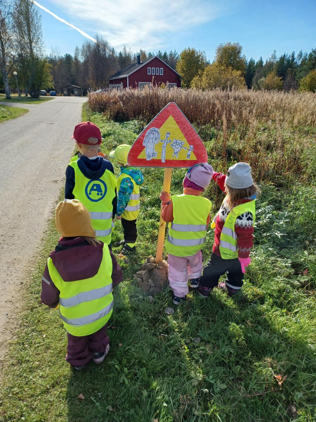 Lapset tienreunassa itsetekemän liikennemerkin kanssa