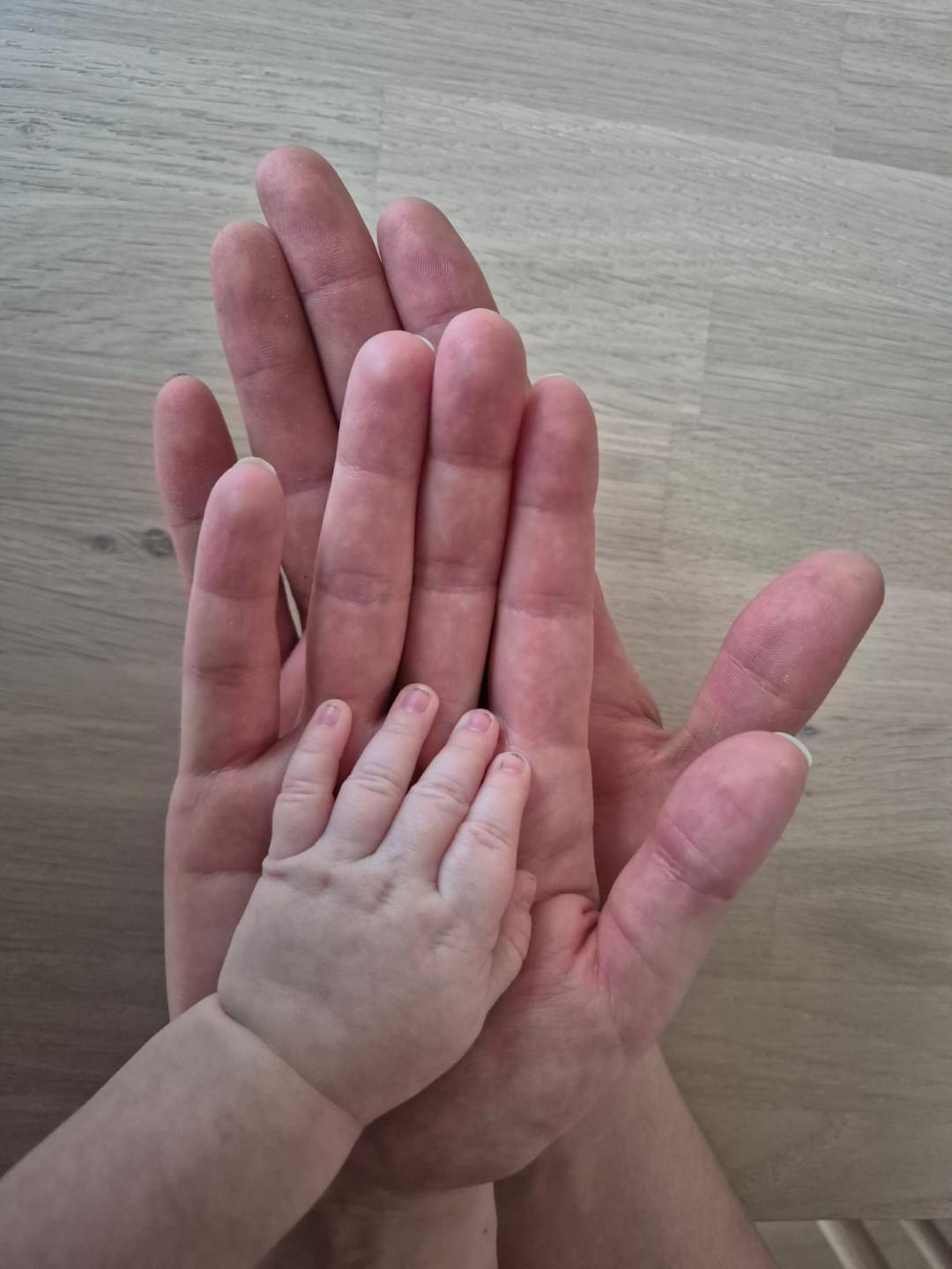Kaksi aikuisen kättä ja vauvan käsi päällekkäin